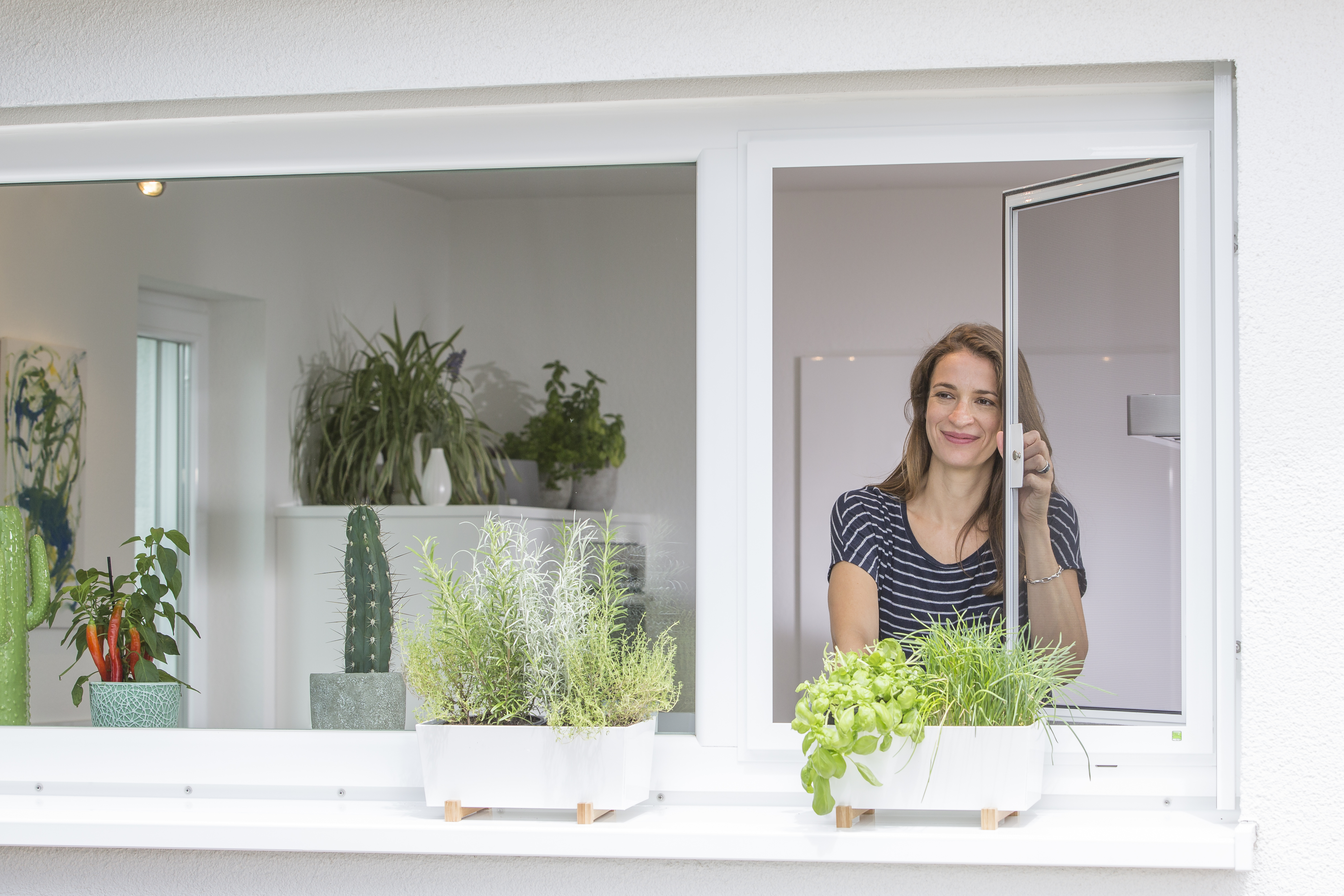 Frau öffnet Fenster mit eingesetztem Insektenschutz-Drehrahmen aus Aluminium
