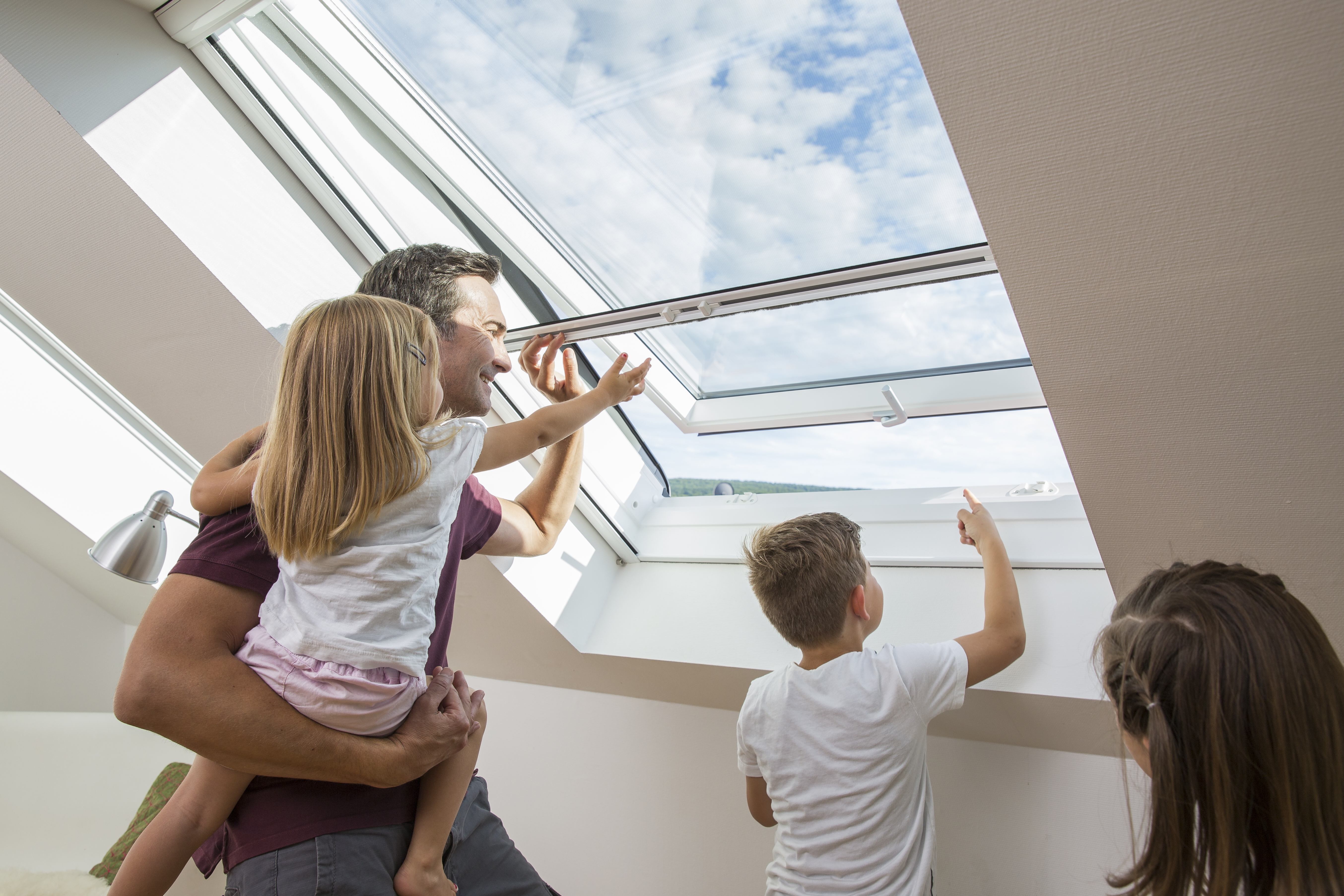 Familie öffnet Dachfenster mit integriertem Insektenschutz-Rollo – frische Luft ohne Insekten