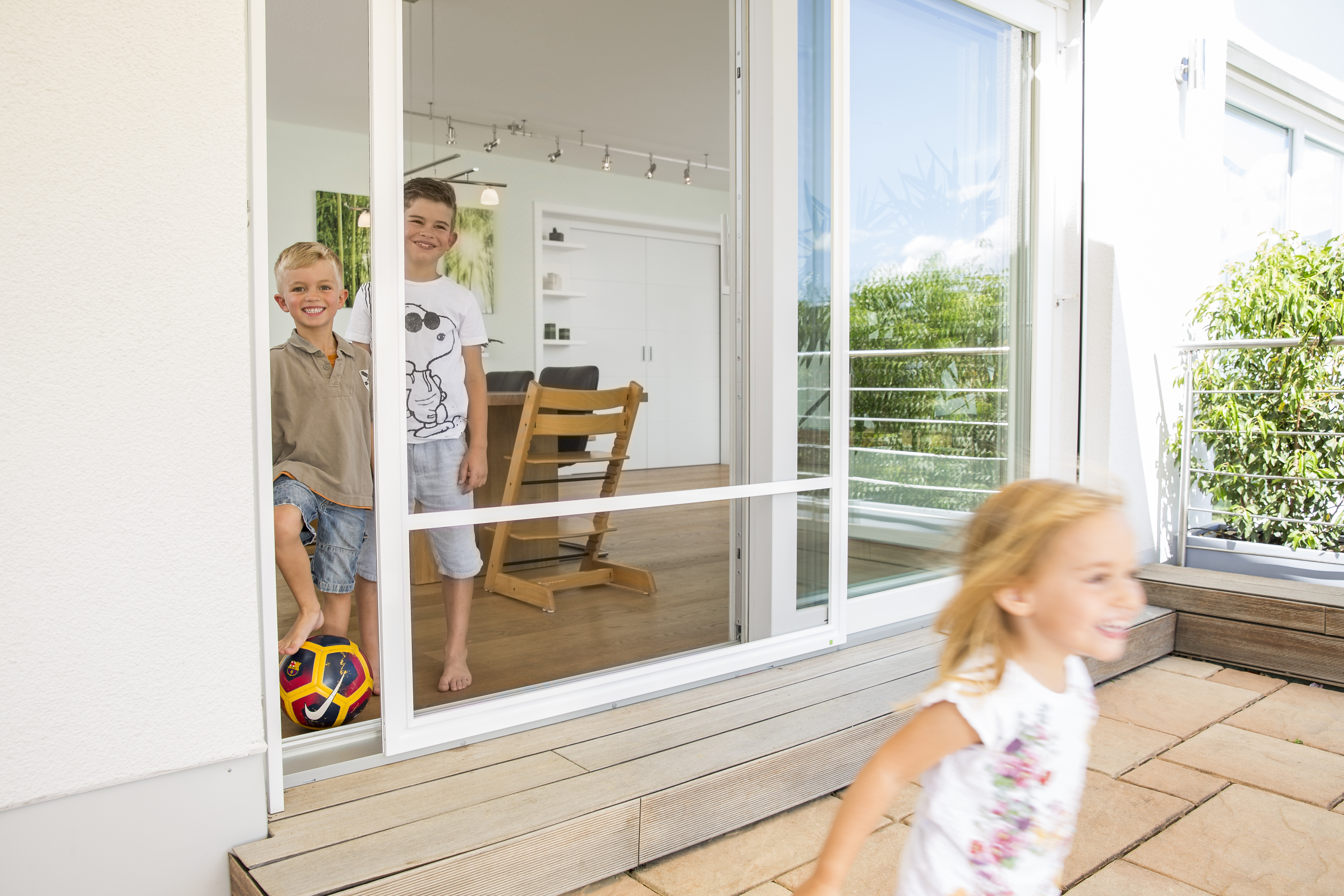 Kinder spielen und treten durch geöffnete Insektenschutz-Schiebetür auf Terrasse