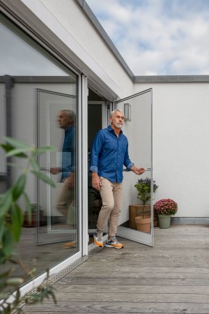 Mann öffnet weiße Insektenschutz-Drehtür an Balkontür – barrierefreier Übergang